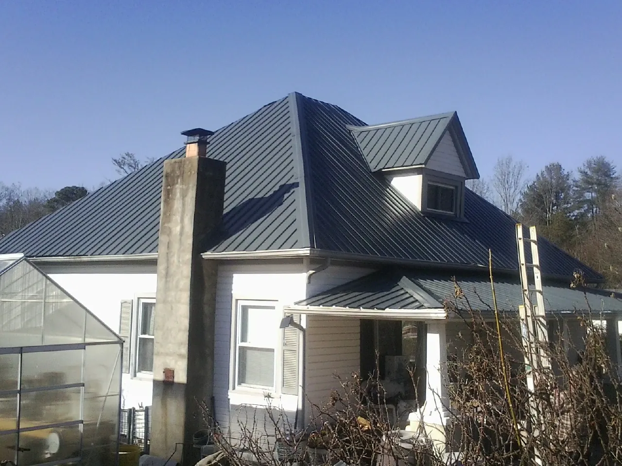 Dark blue standing seam metal roof on a white farmhouse with dormer — Slate & Tile Roof Repair by Roofing Brothers in Story City