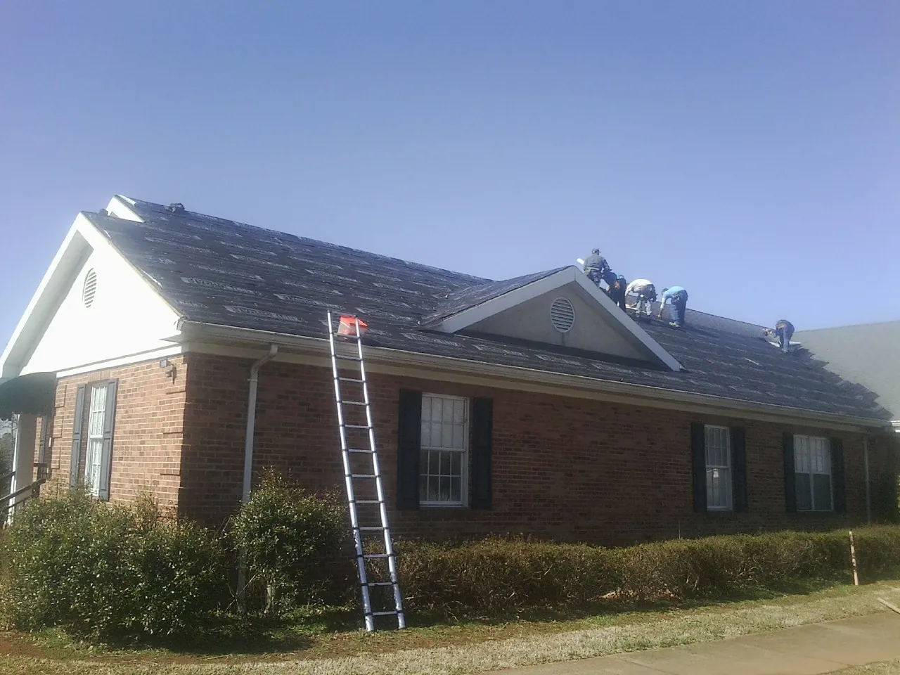 Crew tearing shingles off a brick ranch roof with a ladder set — Metal Roof Repair work by our crew in Story City