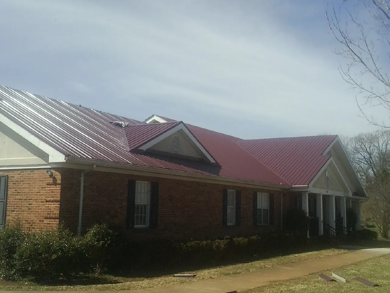 Red metal roof with gabled entries on a long brick building, from a Hail Damage Roof Repair job in Story City