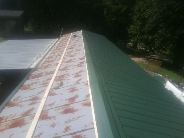 Old rusted panels beside newly installed green metal roofing — Wind Damage Roof Repair by Roofing Brothers in Story City