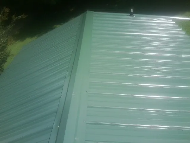 New green metal panels meeting at the ridge of a roof — Flat Roof Repair work by our crew in Story City