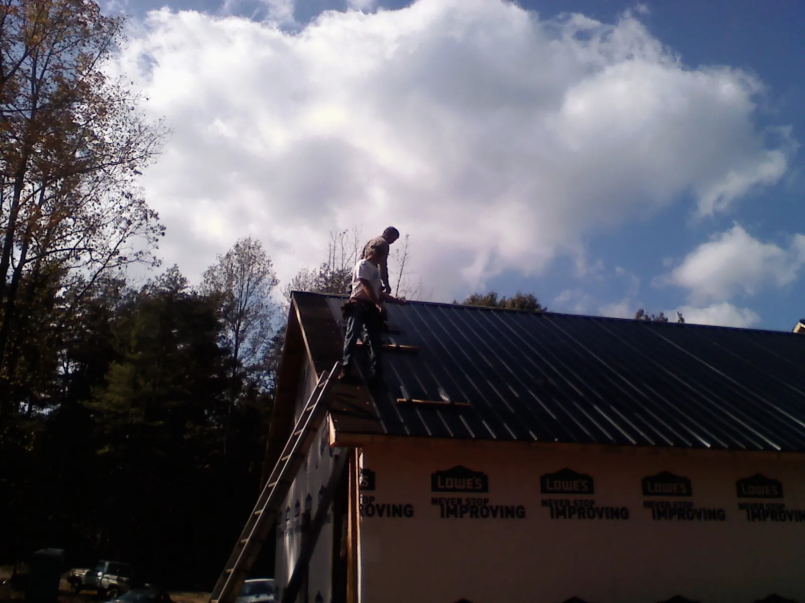 Roofer fastening dark metal panels high against a cloudy sky, from a Roof Inspection job in Story City