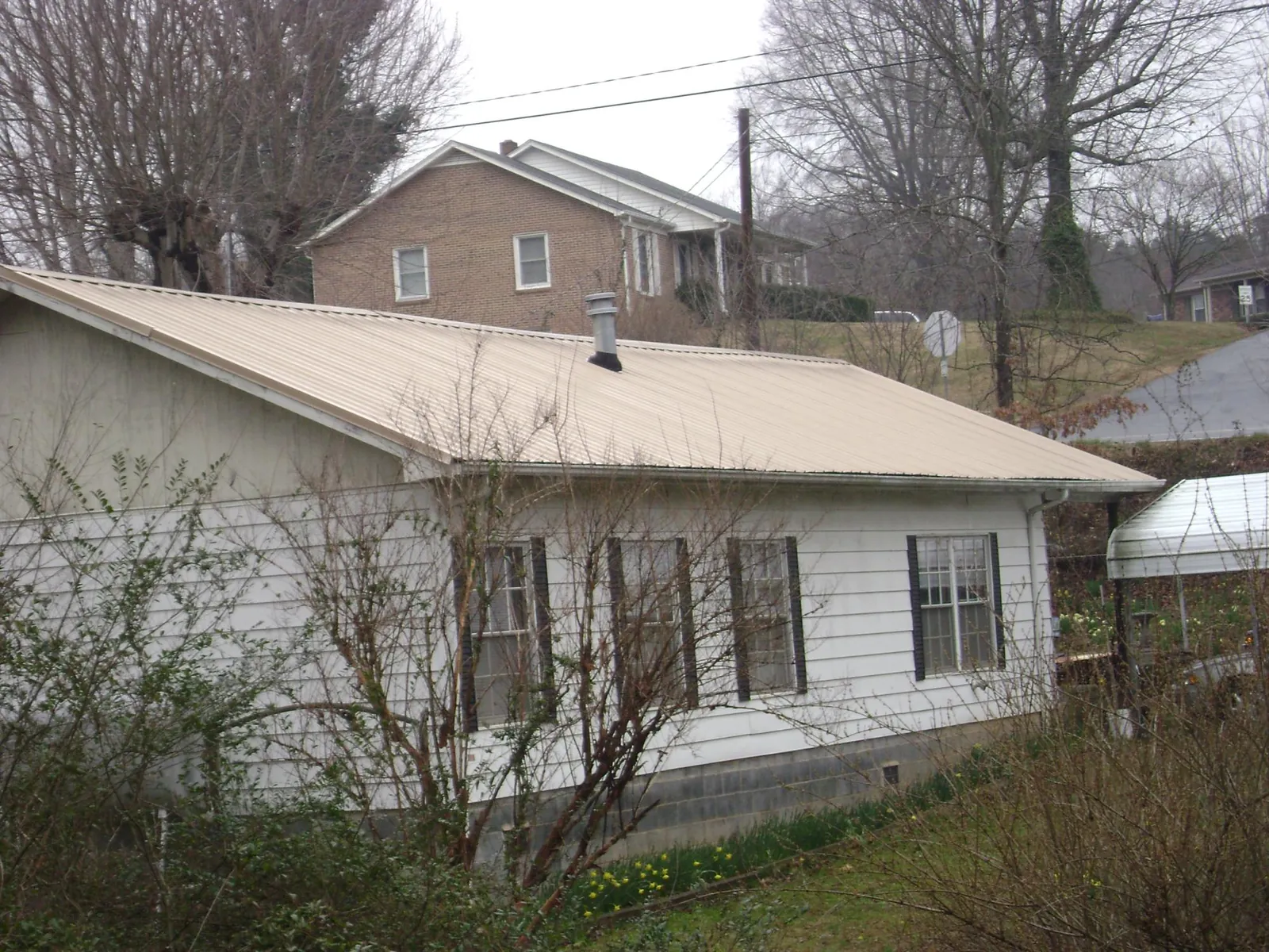 Tan metal roof on a white sided house set into a hillside — Commercial Roofing by Roofing Brothers in Story City